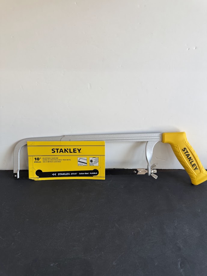Stanley hacksaw with a yellow handle resting on a dark surface, blade exposed and frame laid out along a table edge, ready to cut
