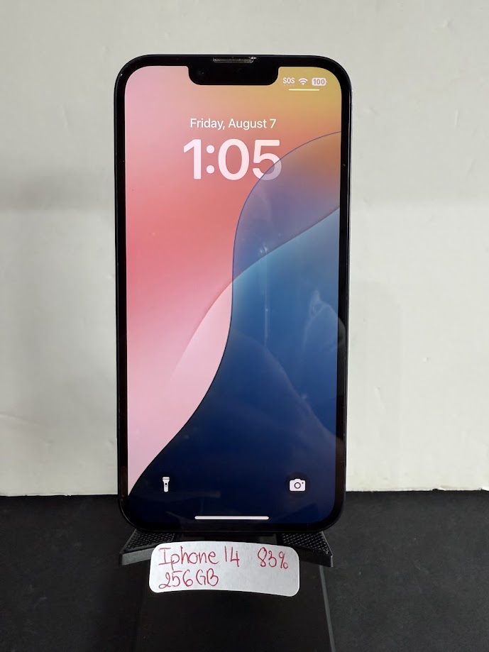 Black iPhone 14 on a display stand, screen shows time 1:05 with colorful wallpaper; handwritten tag below reads 'iPhone 14 256GB 85%'.