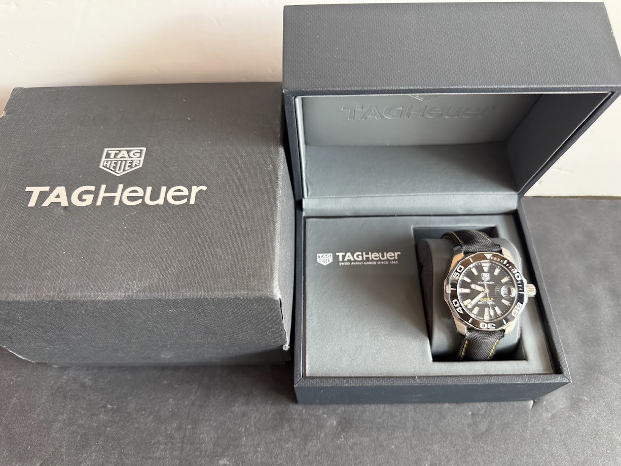 TAG Heuer wristwatch in an open presentation box with a black strap and rotating bezel, in a dark blue outer box.